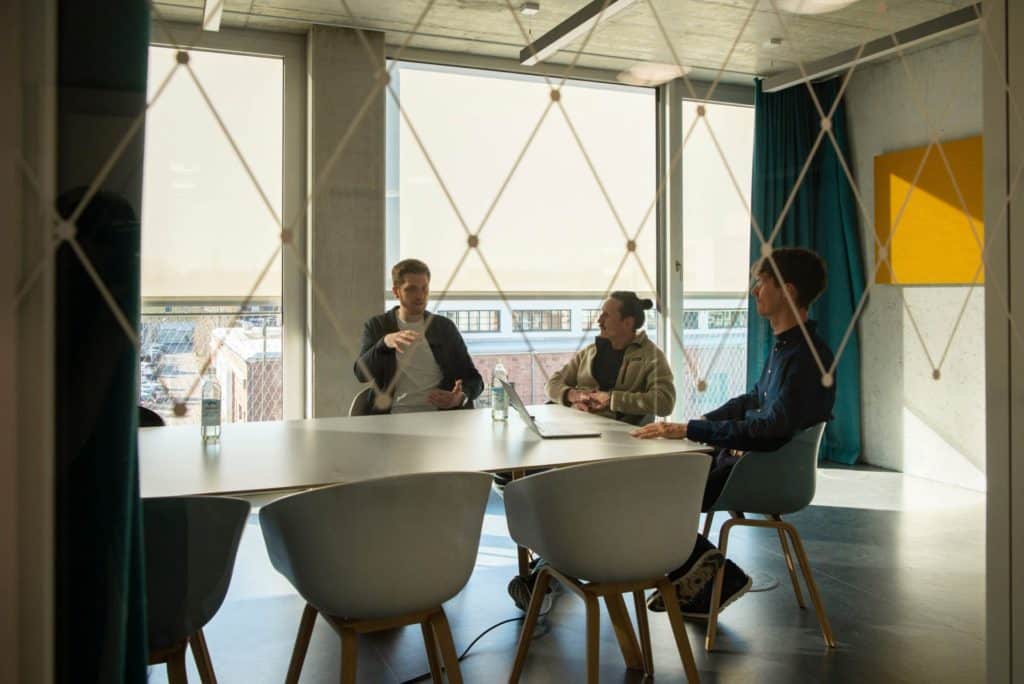 WordPress Agentur Gruppenfoto der dreiQBIK GmbH: Joscha Holzhäuer, Lennart Schleifer und Moritz Bappert diskutieren Entwicklung einer Custom WordPress-Website im Konferenzraum im FUX in Karlsruhe