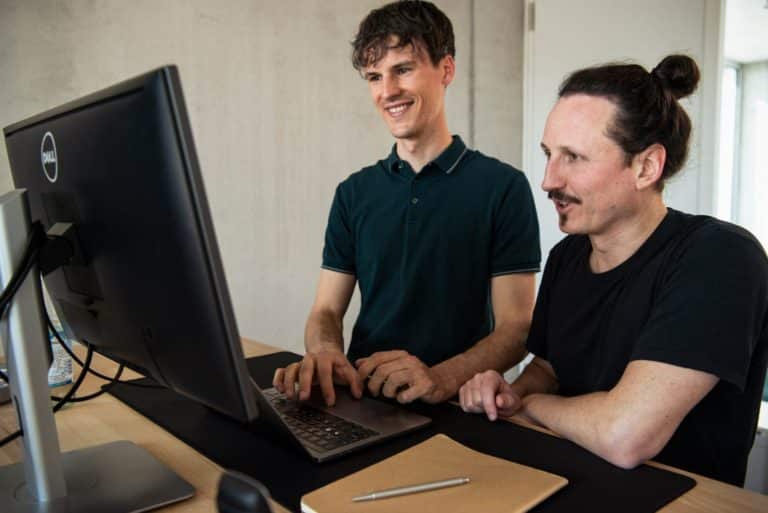 WordPress Agentur Gruppenfoto der dreiQBIK GmbH: Moritz Bappert und Lennart Schleifer im Büro am PC besprechen WordPress-Webdesign - Im Bürokomplex FUX in Karlsruhe